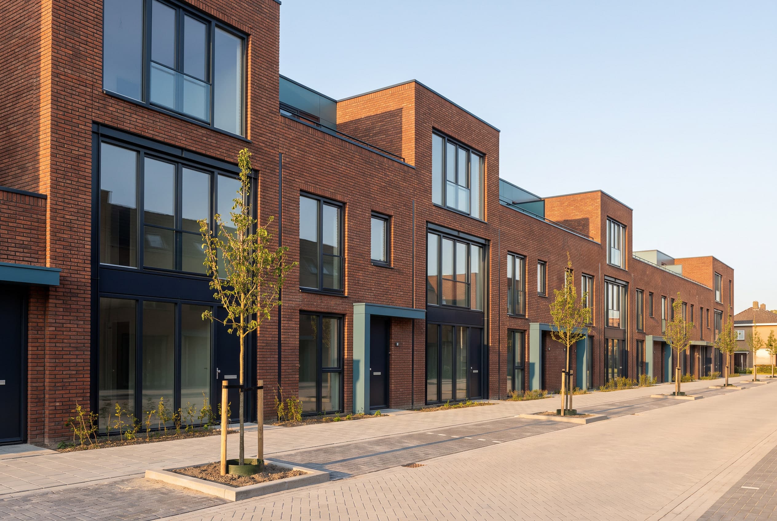 Moderne nieuwbouwwoningen in roodbruine baksteen onder een blauwe lucht.